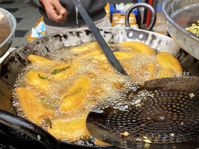 一个不认识的人在煮绿辣椒油饼(mirch pakora)，在大油锅里油炸，印度街头小吃摊贩，印度街头小吃摊档，不健康的饮食，高架视野，重点在前景